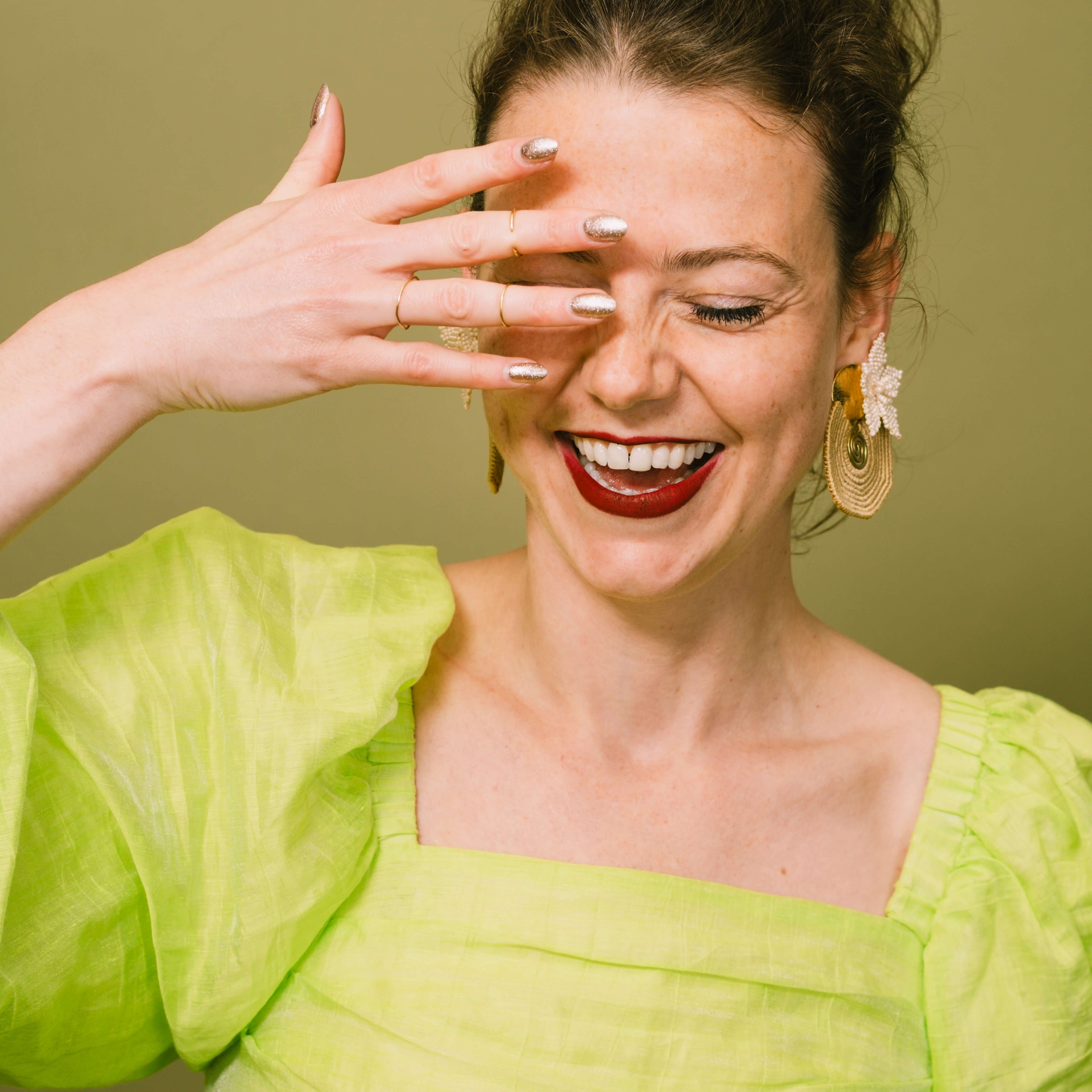 Lachende vrouw met gouden statement oorbellen van TOAIE, in een felgroene blouse