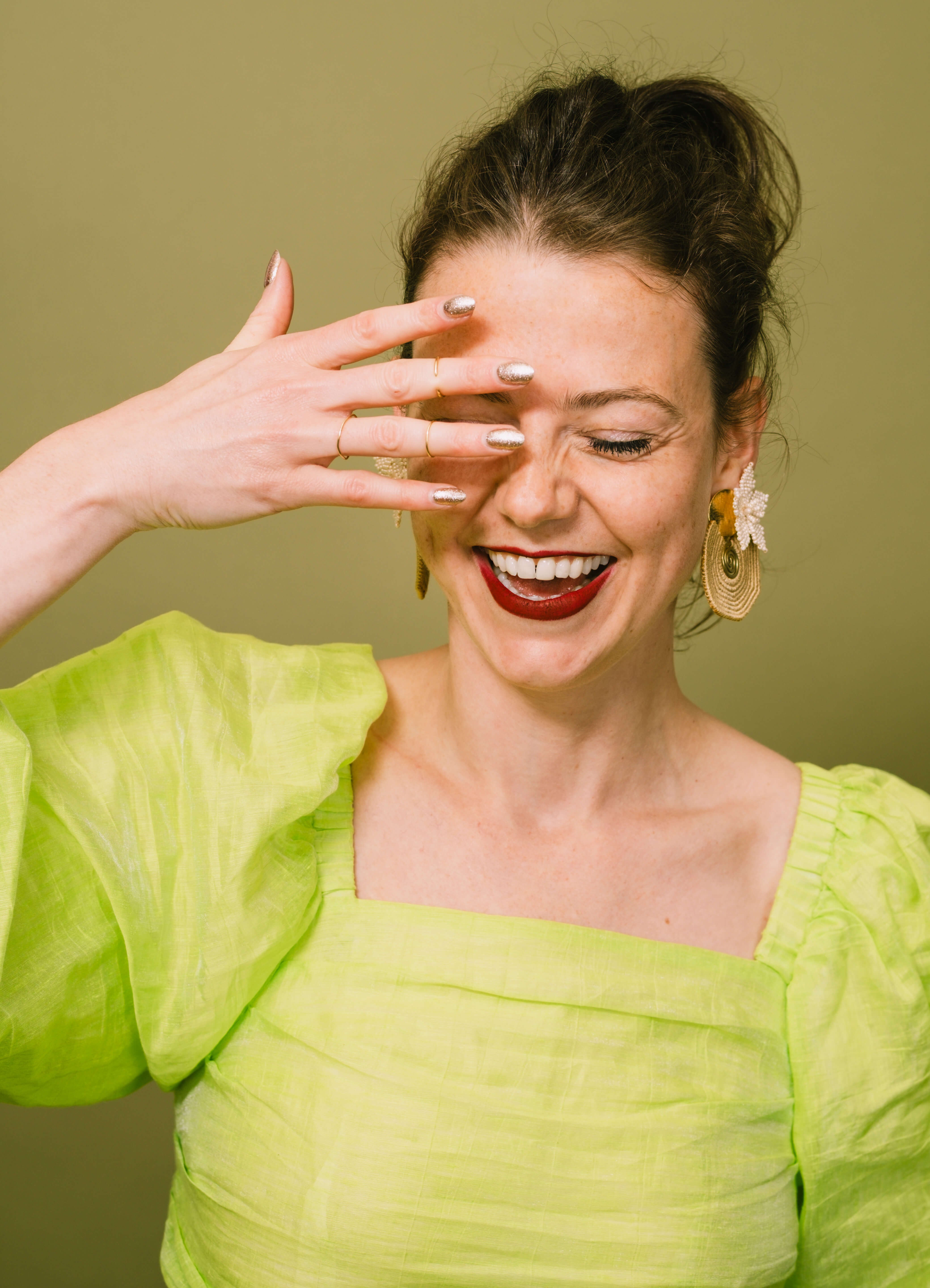 Lachende vrouw met gouden statement oorbellen van TOAIE, in een felgroene blouse
