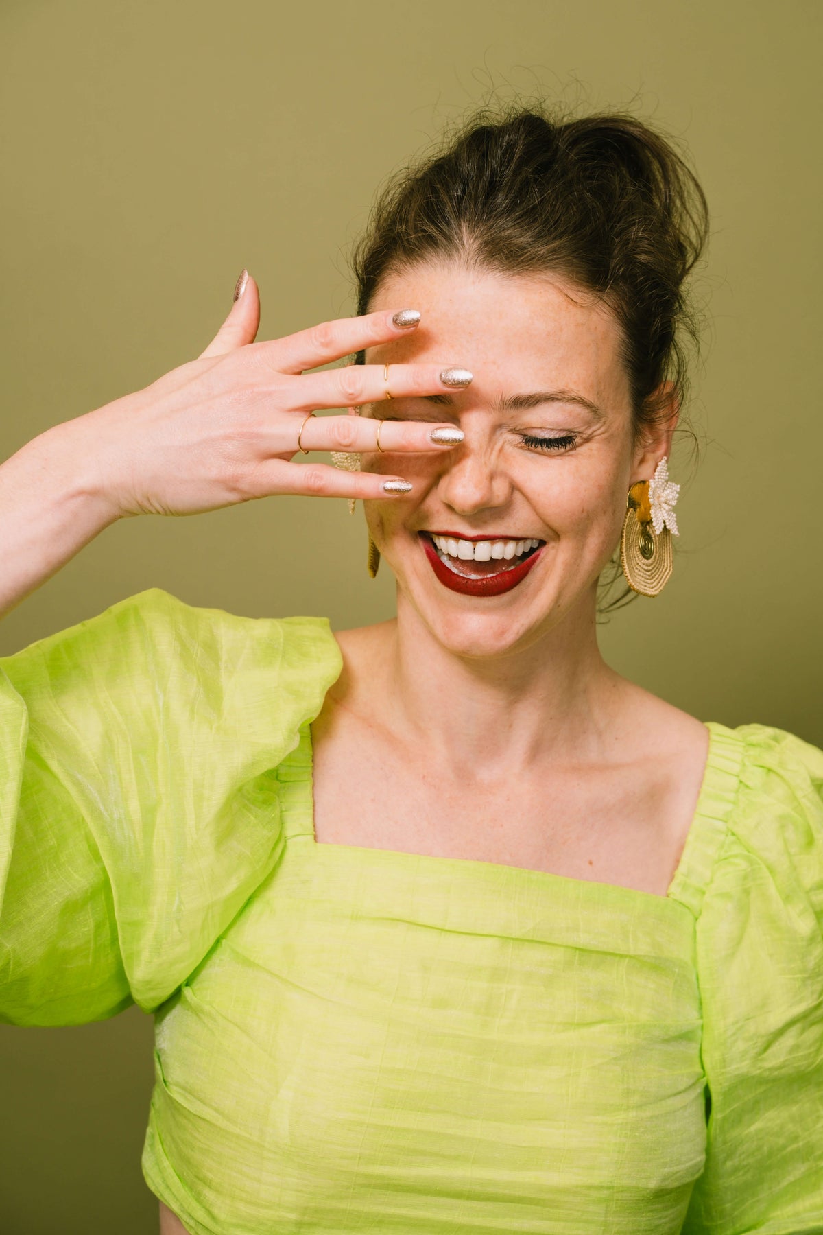 Lachende vrouw met gouden statement oorbellen van TOAIE, in een felgroene blouse