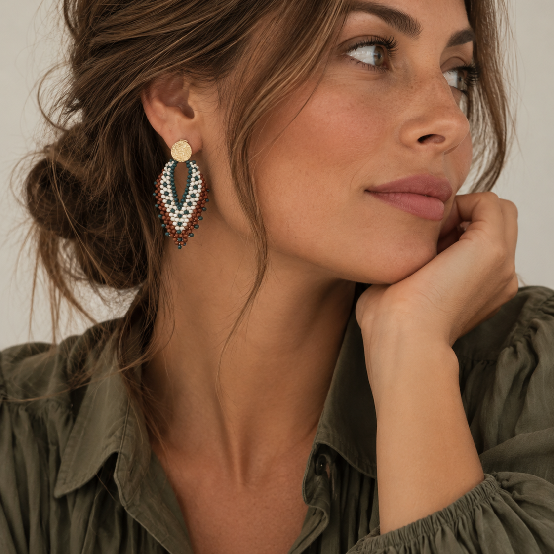 Vrouw draagt The Nomad, lichtgewicht statement oorbellen in bruin/kaki met parelaccenten, handgemaakt in Colombia