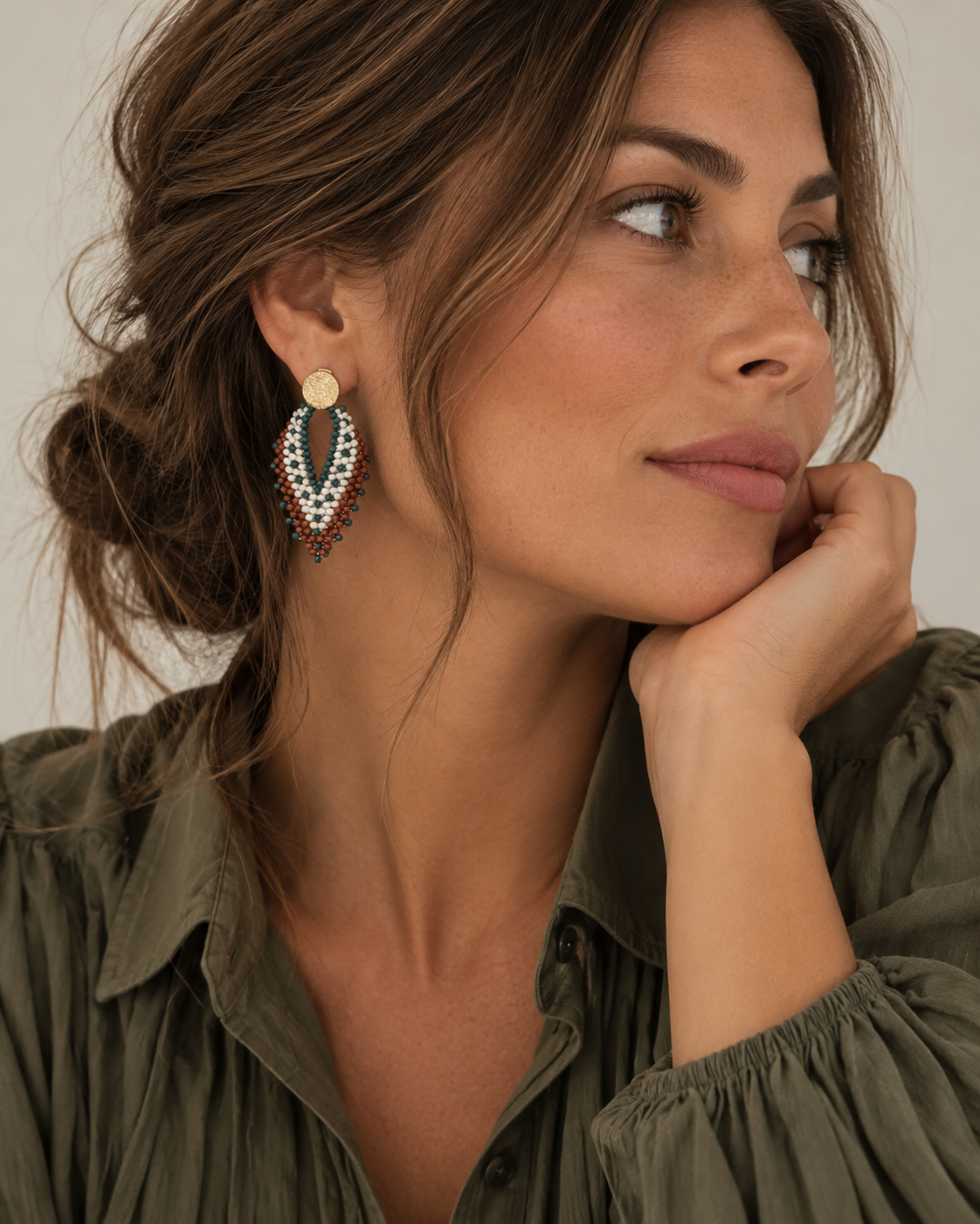 Vrouw draagt The Nomad, lichtgewicht statement oorbellen in bruin/kaki met parelaccenten, handgemaakt in Colombia