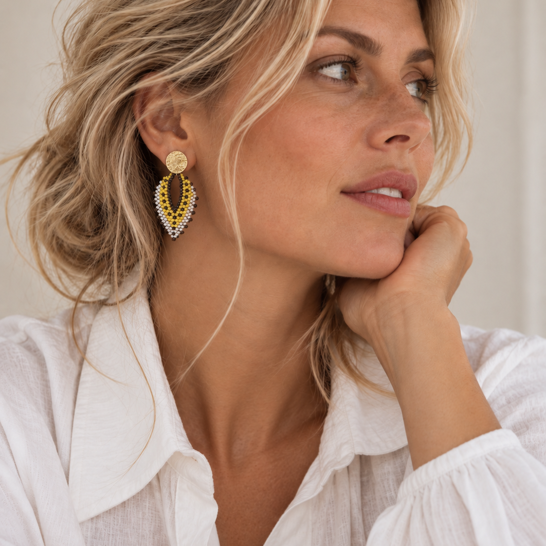Vrouw draagt The Nomad, lichtgewicht statement oorbellen in geeltinten met parelaccenten, handgemaakt in Colombia
