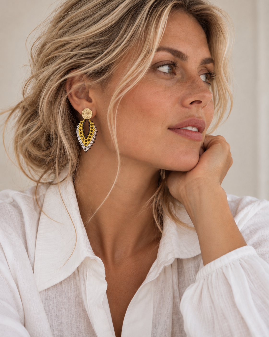 Vrouw draagt The Nomad, lichtgewicht statement oorbellen in geeltinten met parelaccenten, handgemaakt in Colombia